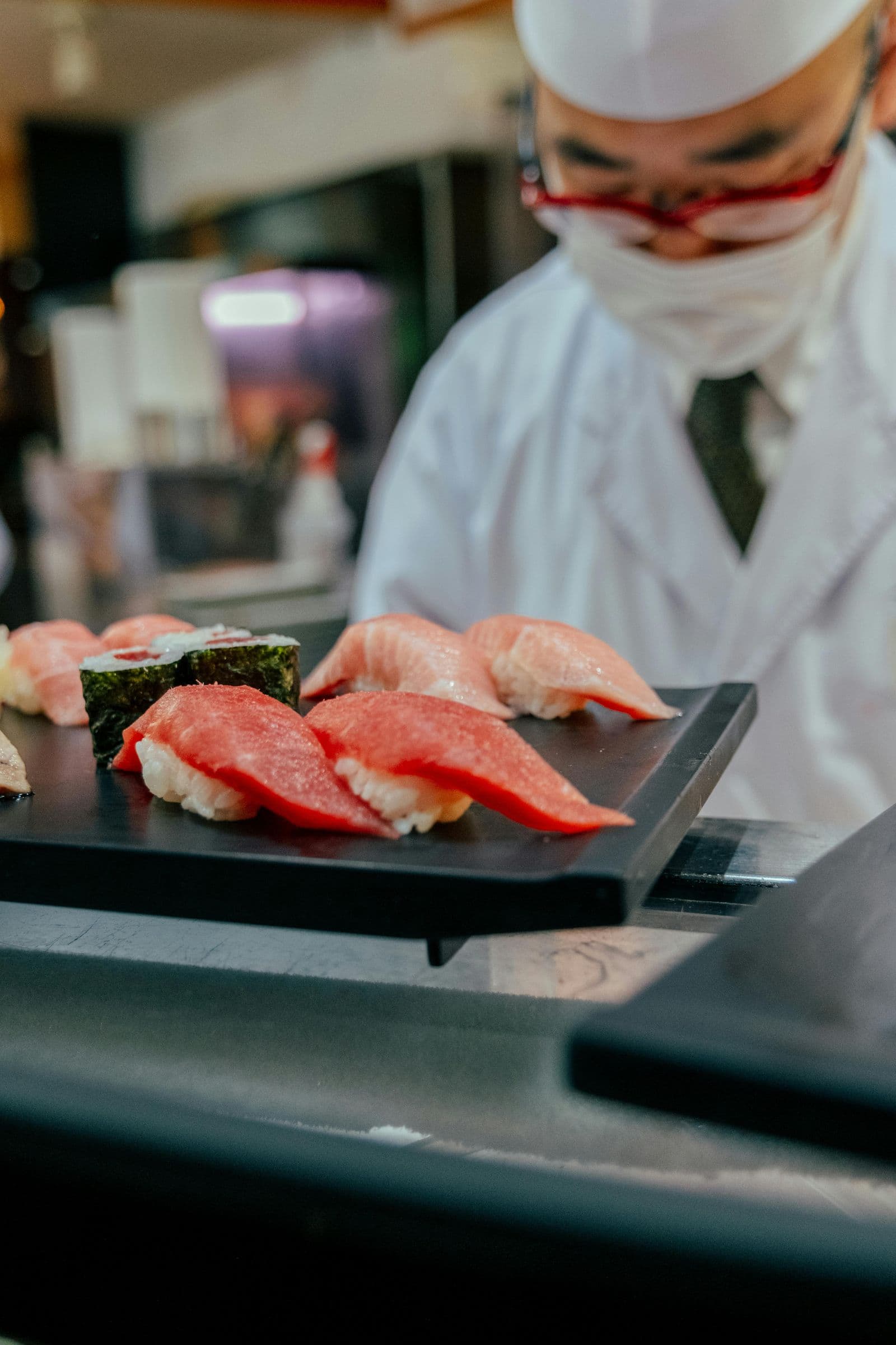 Sushi chef presenting fresh nigiri on black slate — birthday indulgence at an intimate counter