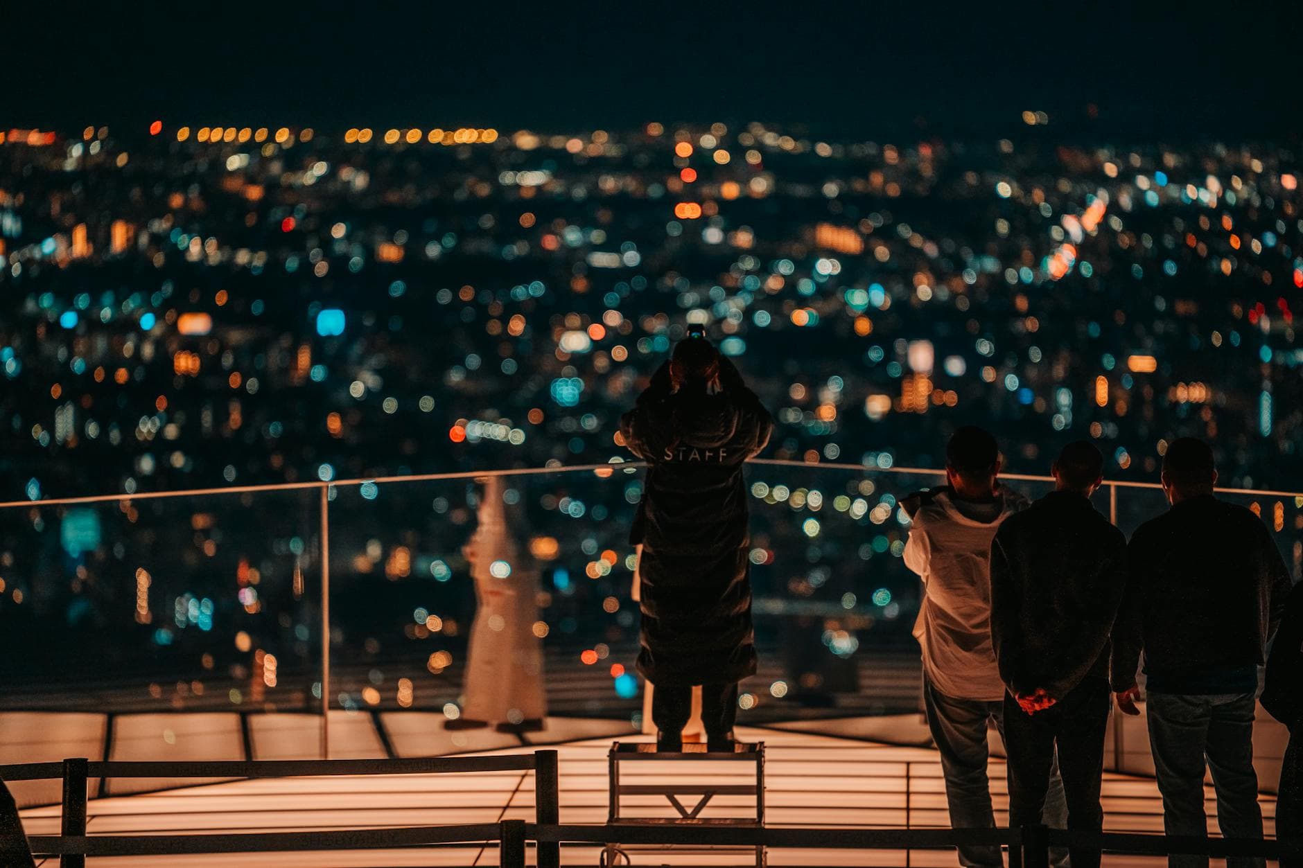 Group of people overlooking Tokyo's glittering nighttime cityscape from a rooftop