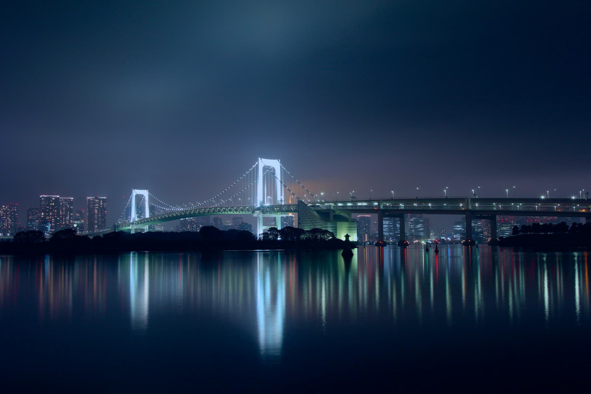 Tokyo Rainbow Bridge illuminated at night with city skyline reflected in the bay