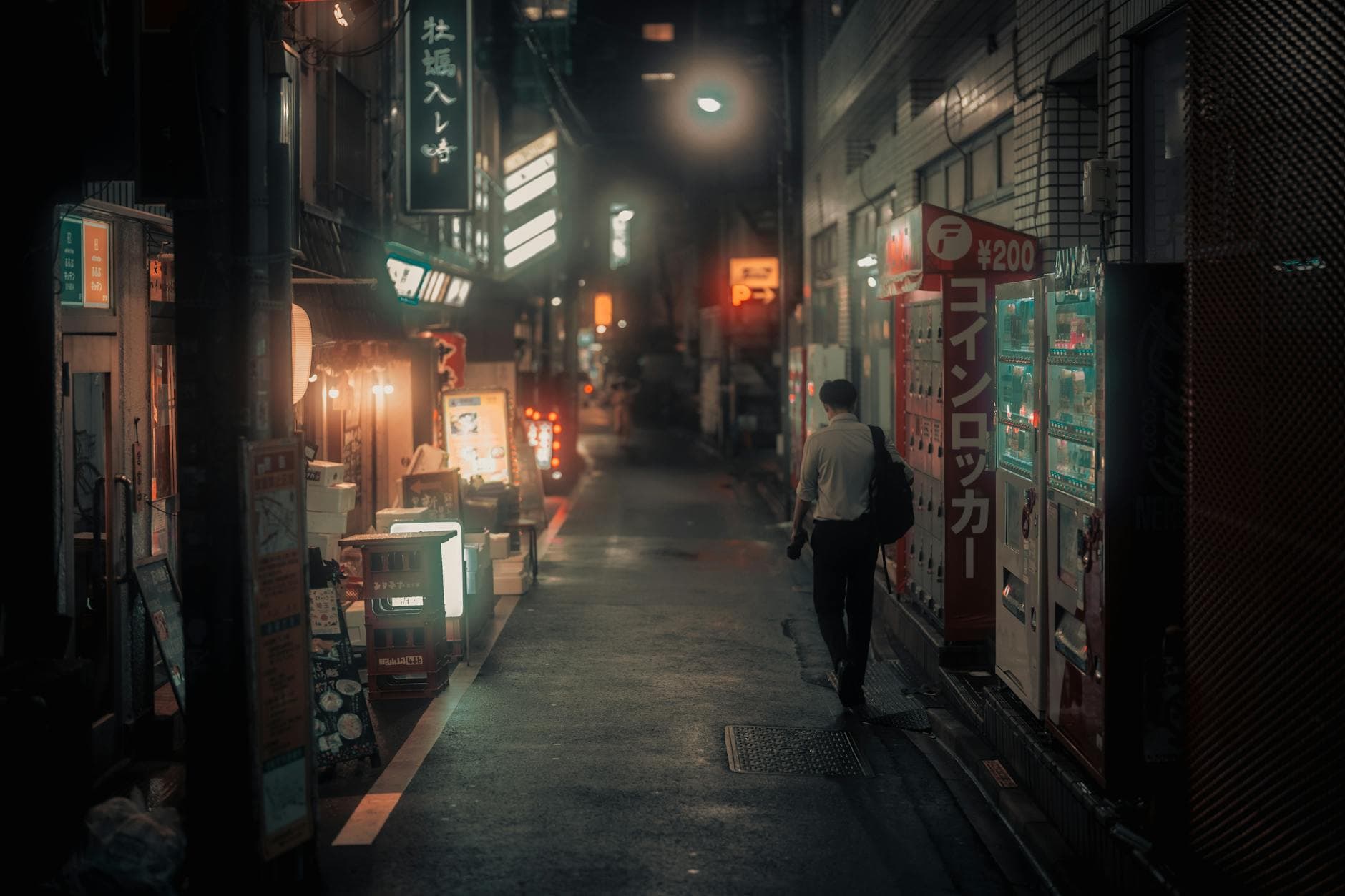 Person strolling through an illuminated narrow alley in Tokyo at night