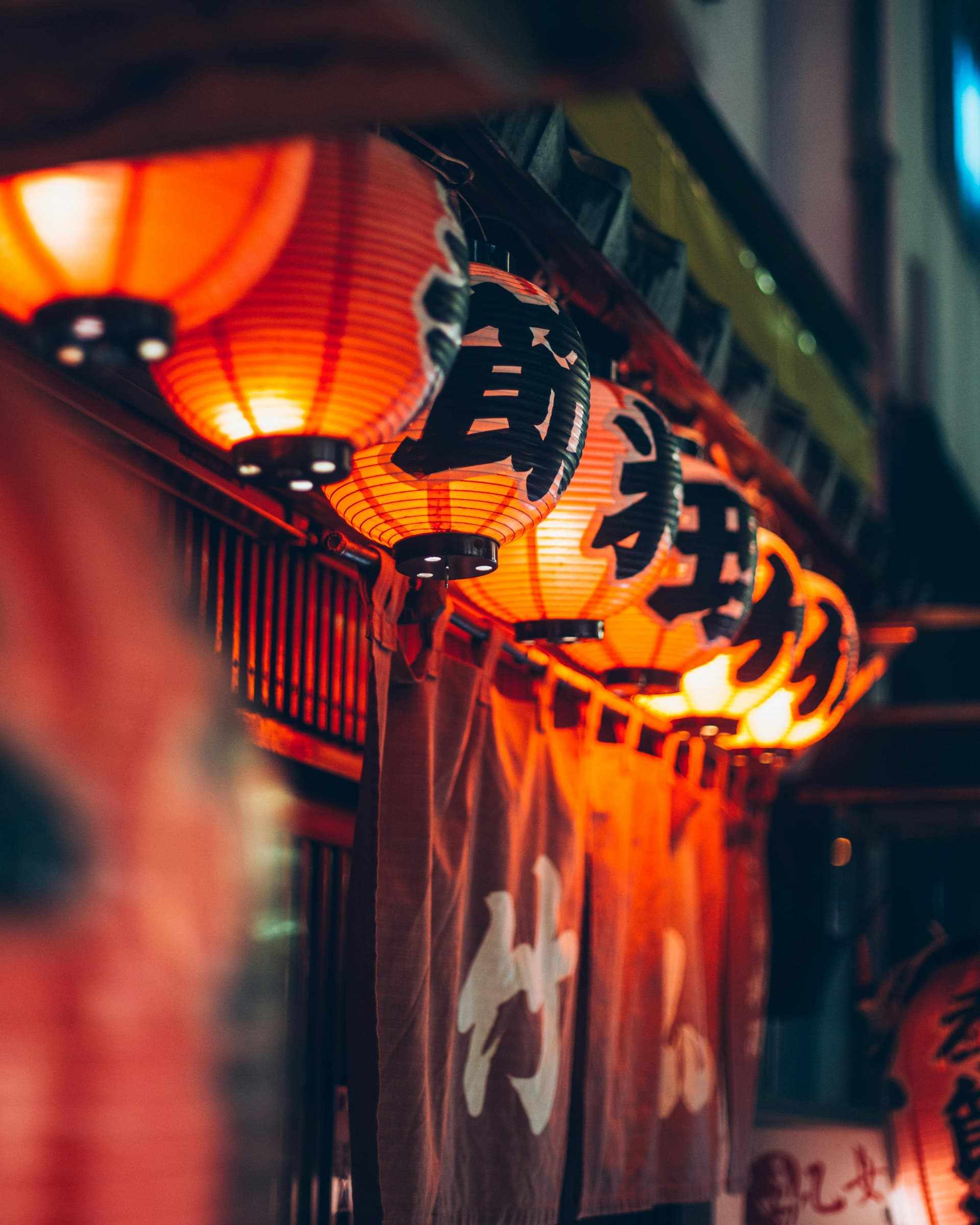 Glowing red paper lanterns strung along an izakaya alley at night