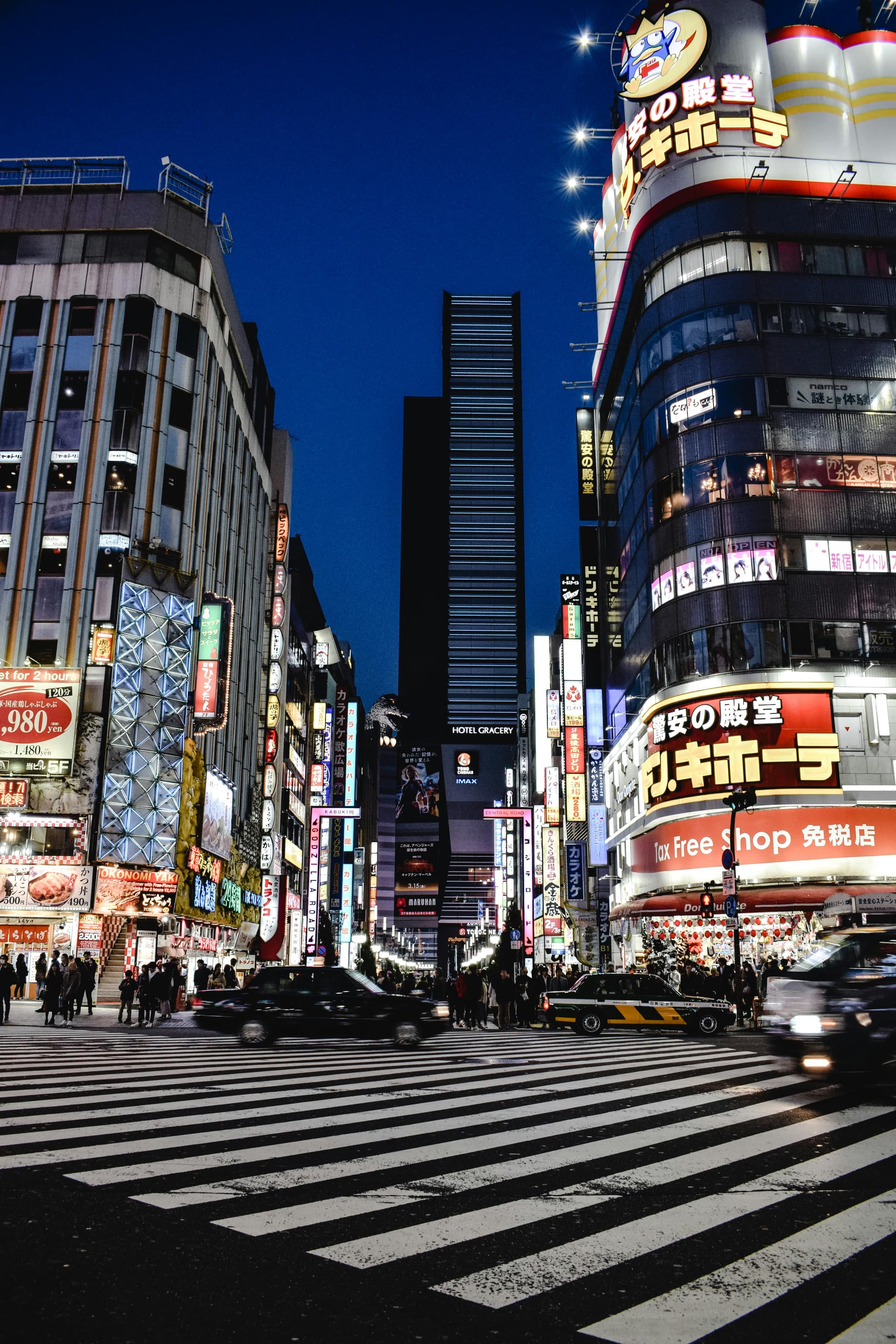 Shinjuku neon night with taxis crossing a wide intersection under illuminated signage