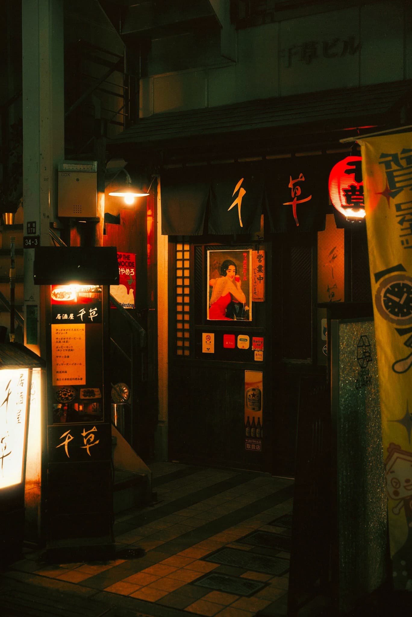 Dark izakaya storefront with vintage poster and single glowing lantern