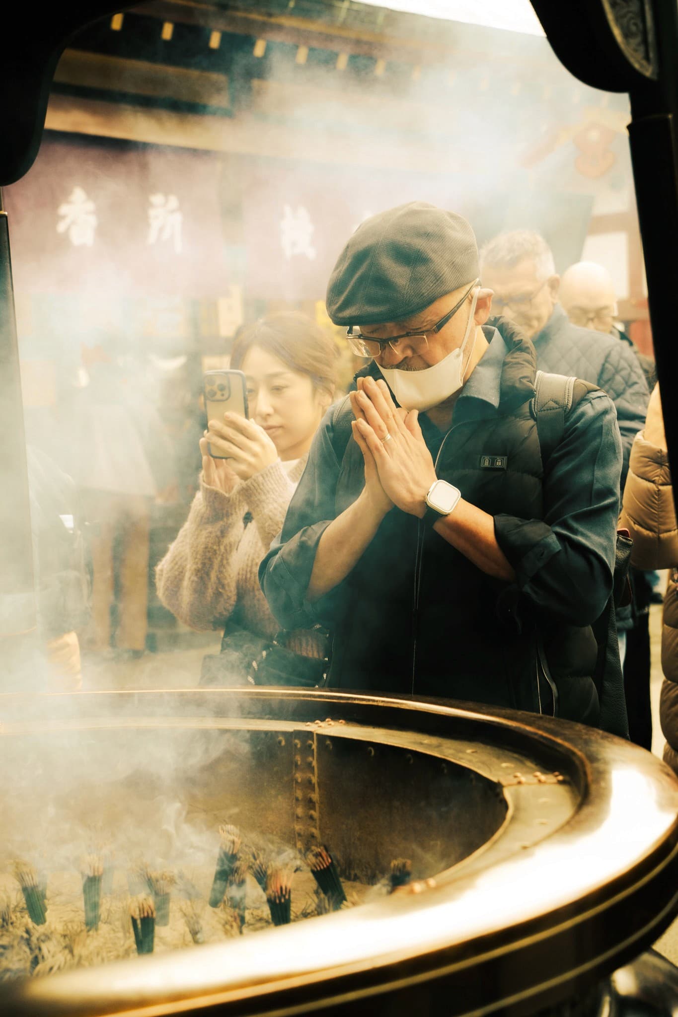 Man praying with clasped hands over incense smoke at a temple brazier