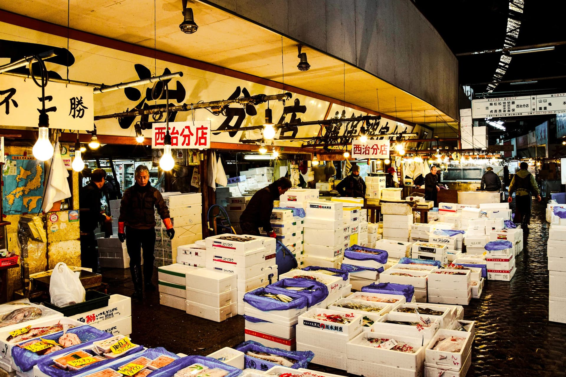 Fish market hall with workers moving crates of fresh seafood under bright lights