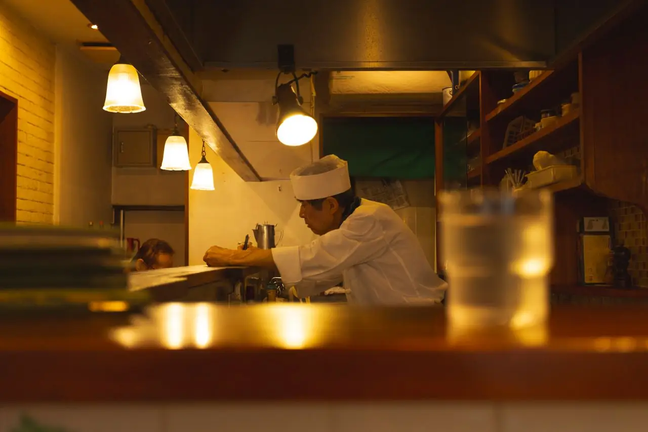Chef working behind the wooden counter of a small, warmly lit restaurant