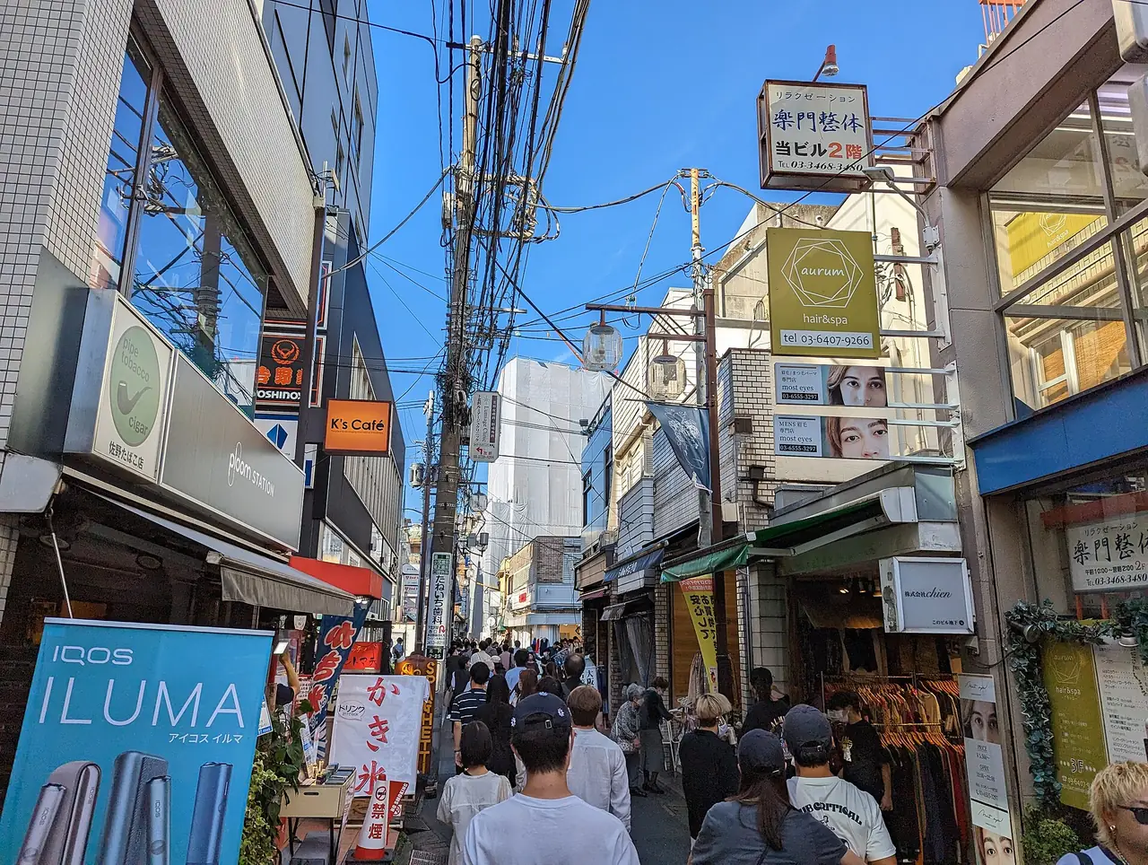 Pedestrians on a narrow shop-lined street in Shimokitazawa on a sunny day