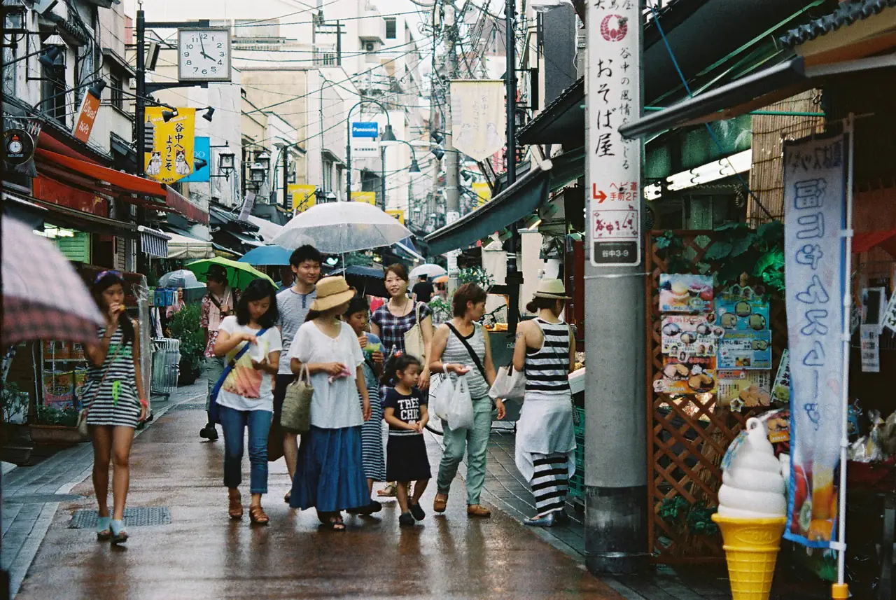 Shoppers with umbrellas browsing small shops along Yanaka Ginza on a rainy day
