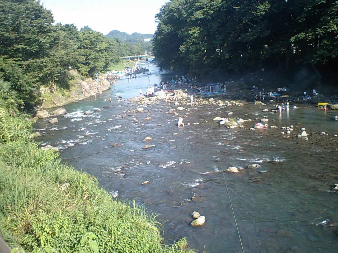Families wading among rocks in the shallow, clear Akigawa River on a summer day