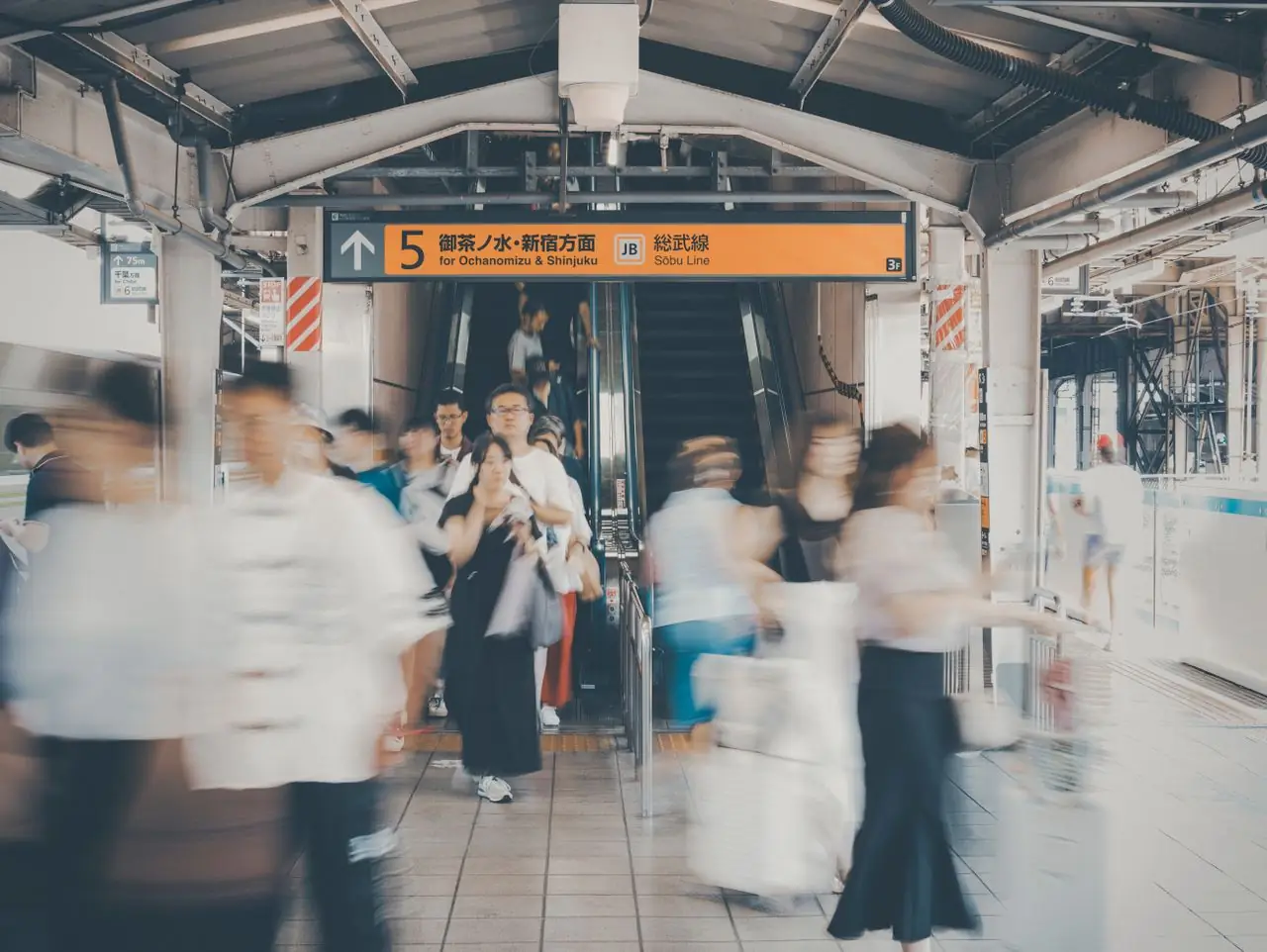 Commuters hurrying past an escalator under a Sobu Line platform sign in Tokyo