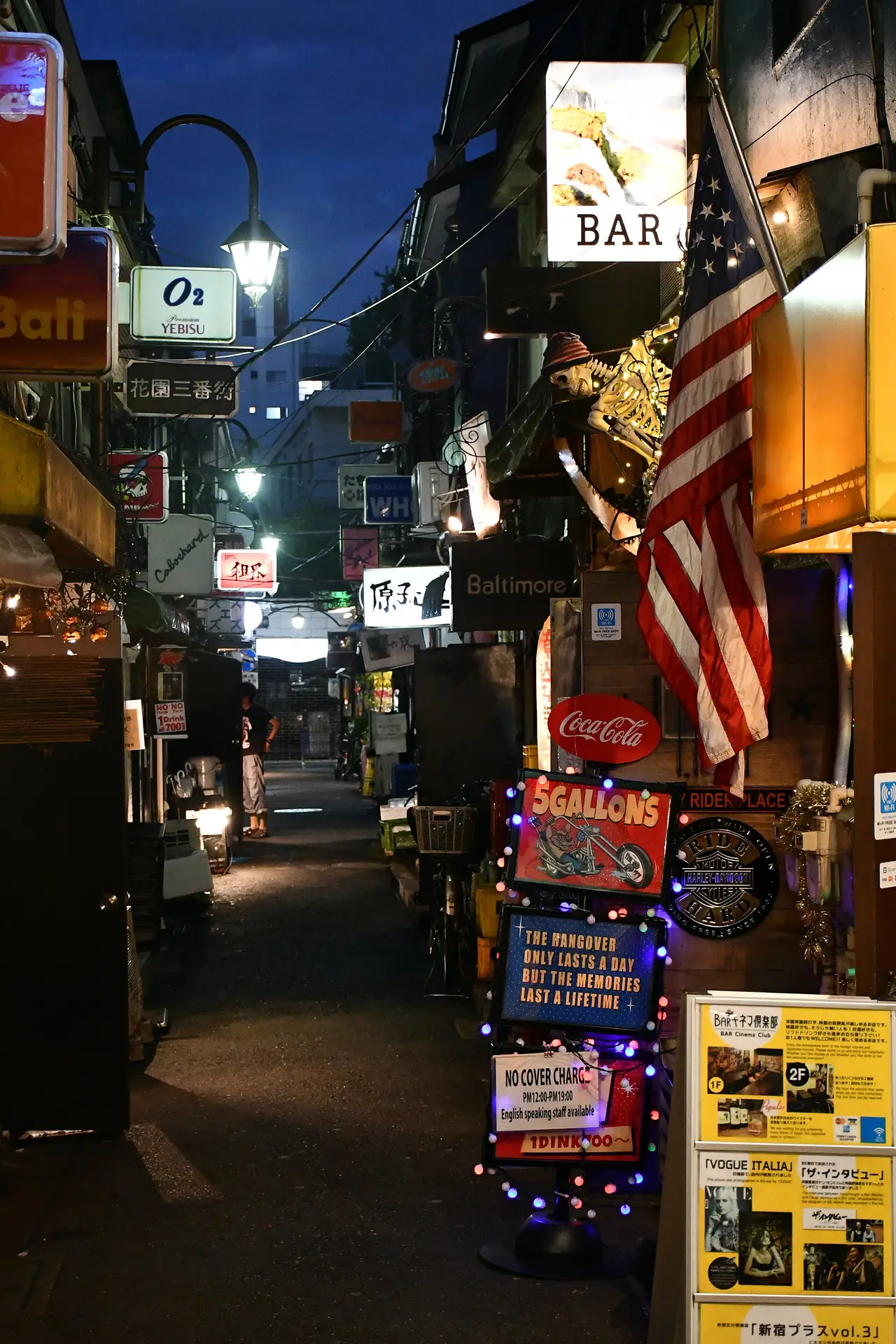 Bar signs and a no cover charge board in a Golden Gai alley at dusk