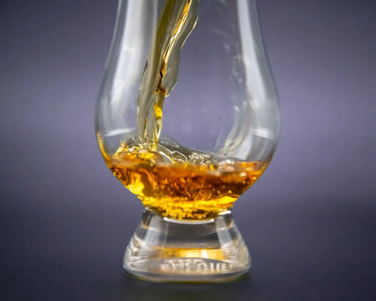 Amber whisky being poured into a tulip-shaped nosing glass