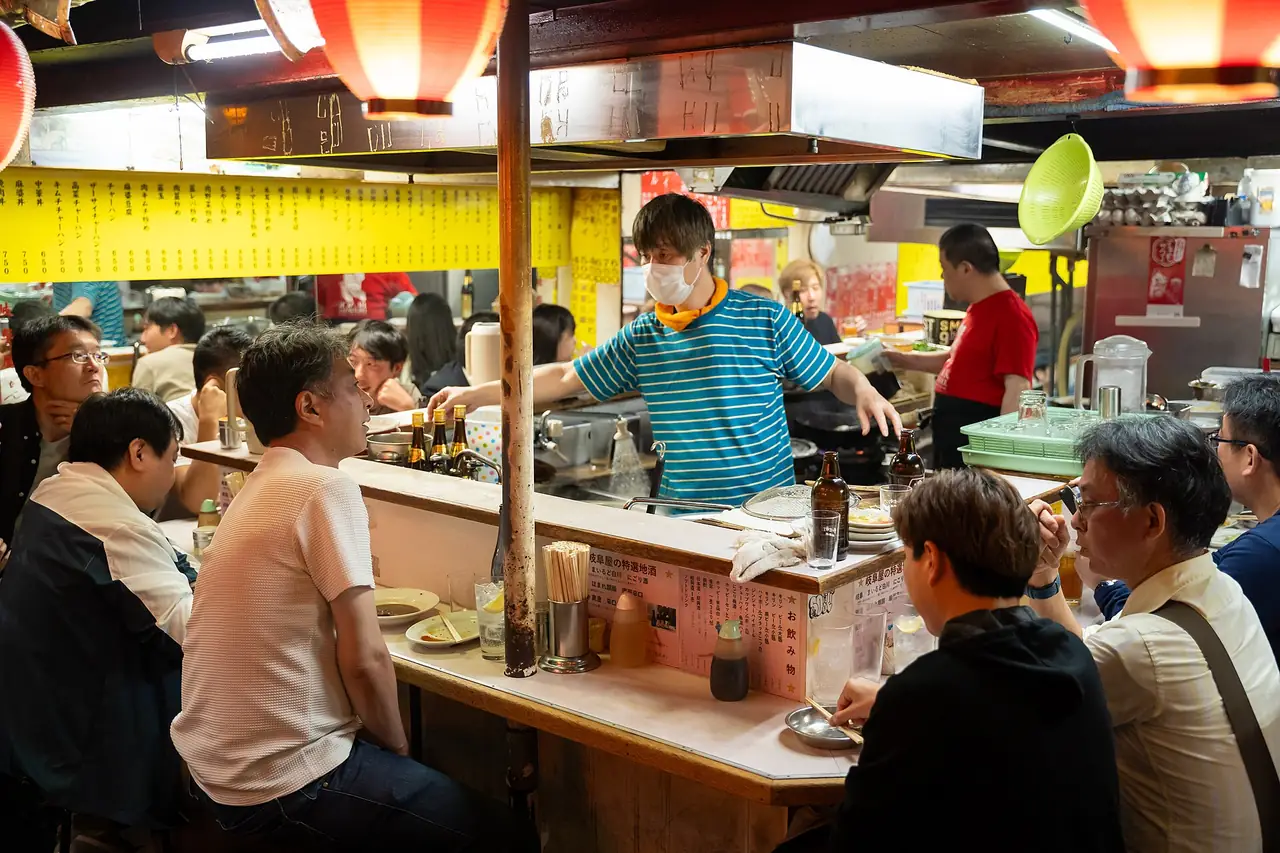 Diners at a small counter bar with handwritten Japanese menus in Omoide Yokocho, Shinjuku