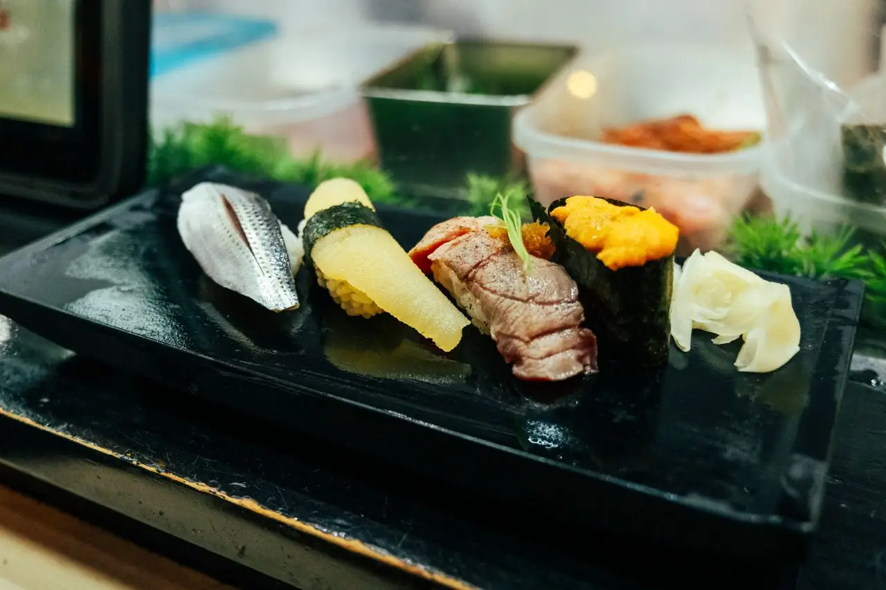 Four pieces of nigiri including sea urchin on a black plate at a Tokyo sushi bar