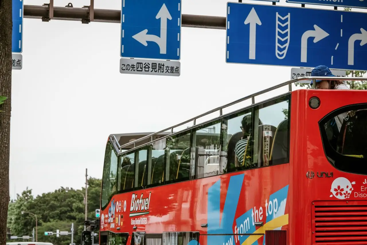 Red open-top sightseeing bus with passengers on a Tokyo street near Yotsuya