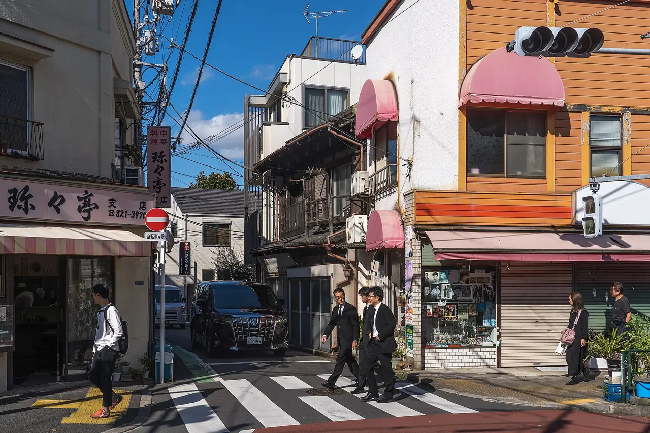 People crossing a quiet street corner lined with old shops in Tokyo's Yanaka district