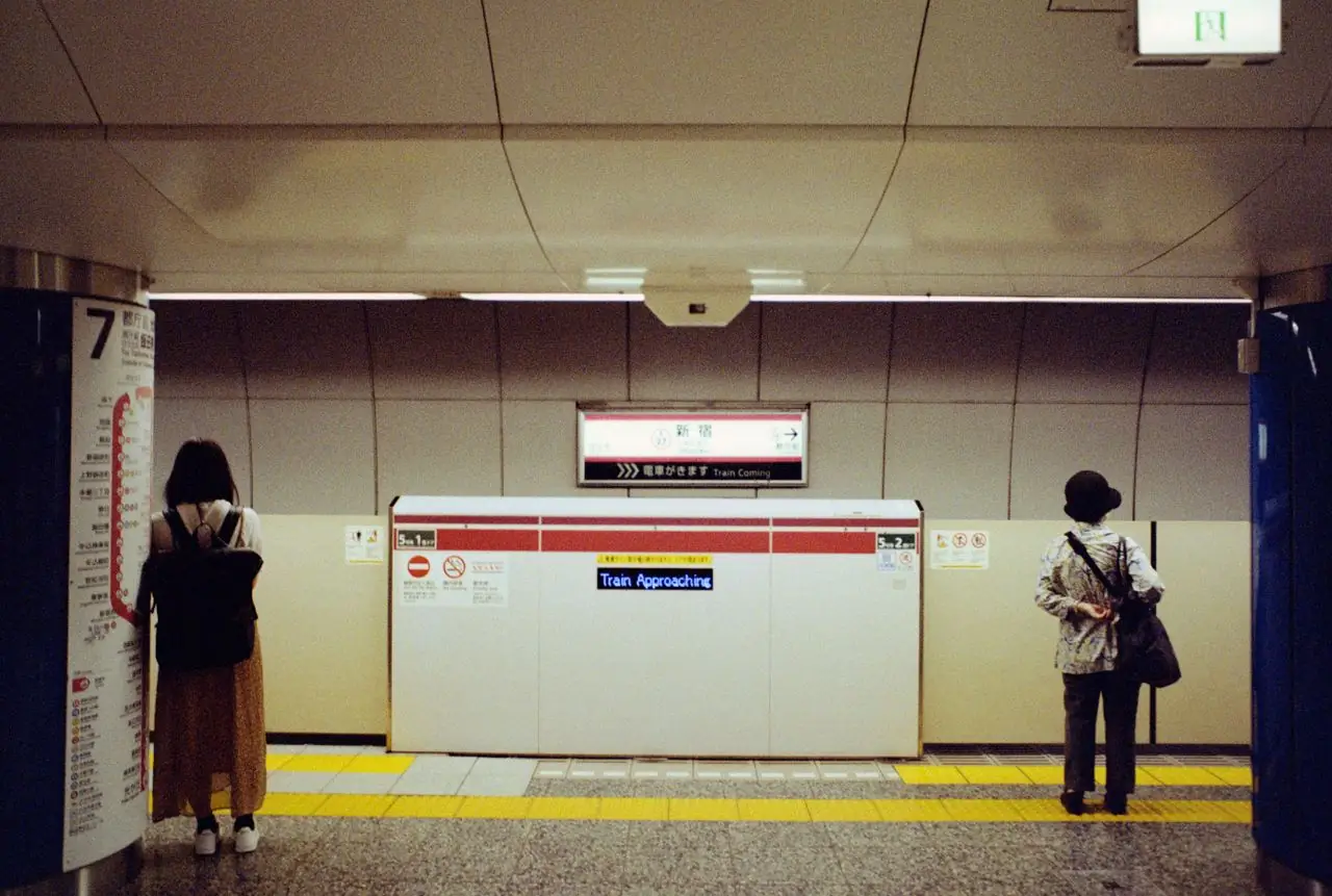 Passengers waiting on a Tokyo subway platform beside an English Train Approaching sign