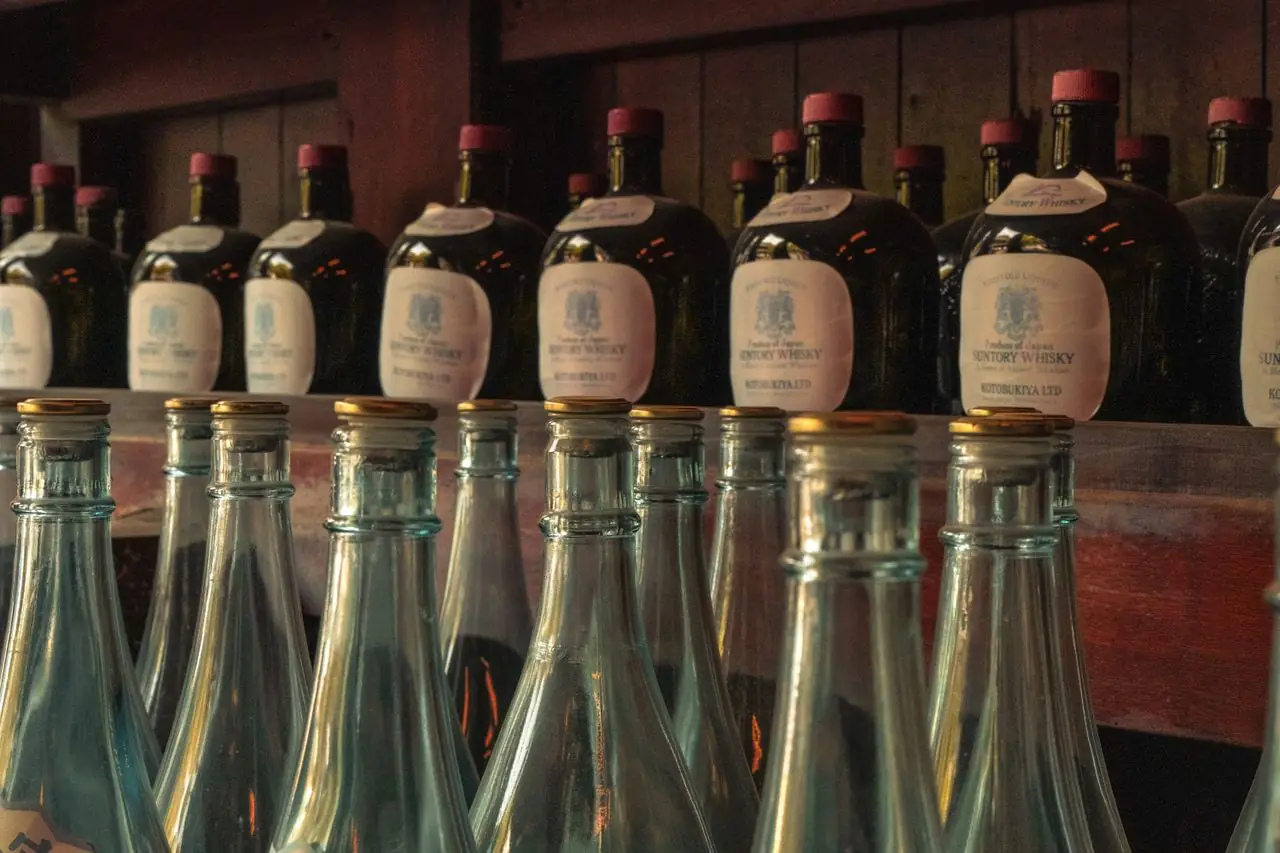 Vintage Suntory whisky bottles on a wooden shelf above empty glass bottles