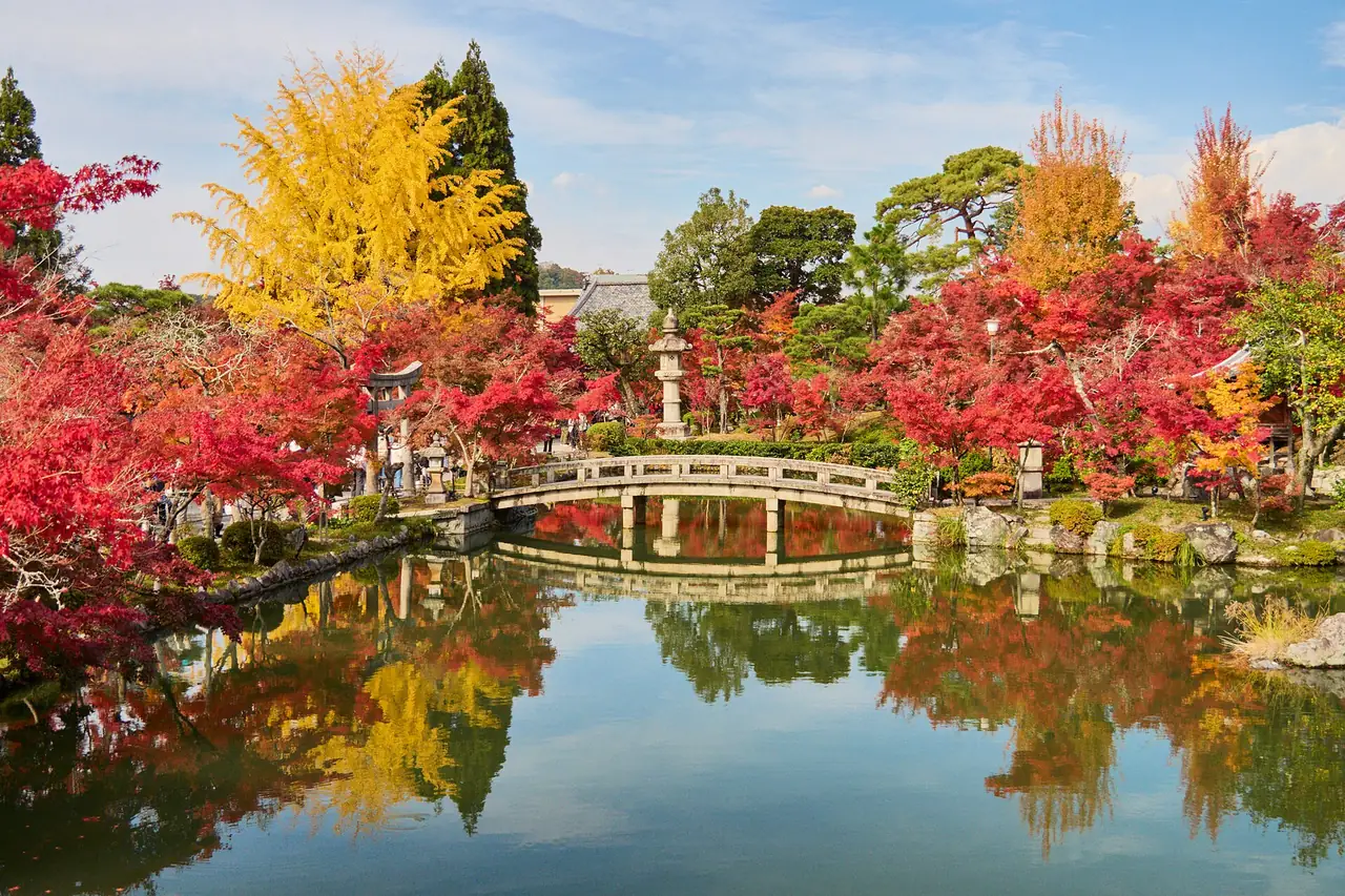 Red maples and yellow ginkgo around the pond and stone bridge at Eikando temple in Kyoto