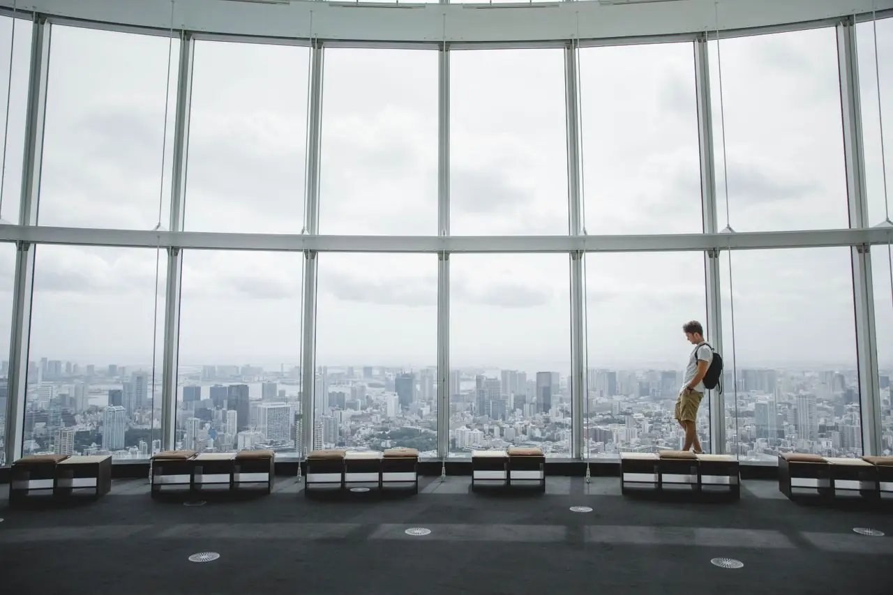 A visitor looking out over Tokyo from the tall curved windows of an observation deck