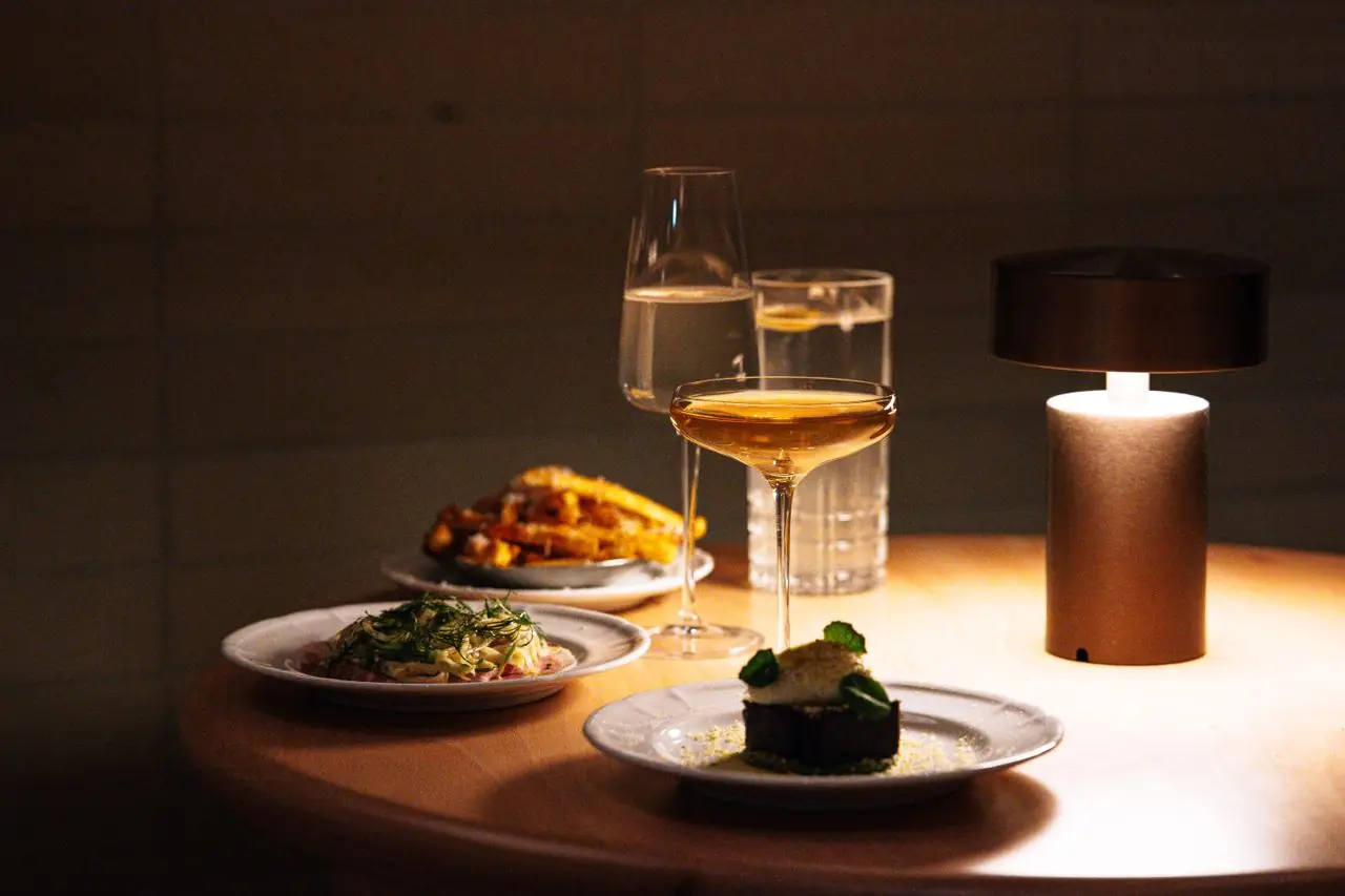Glass of wine and small plates under a table lamp at a wine bar