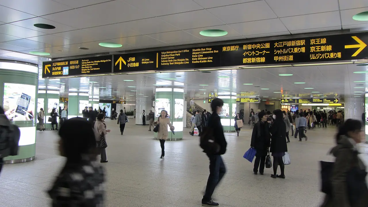 Commuters crossing the underground concourse at Shinjuku Station beneath exit signs