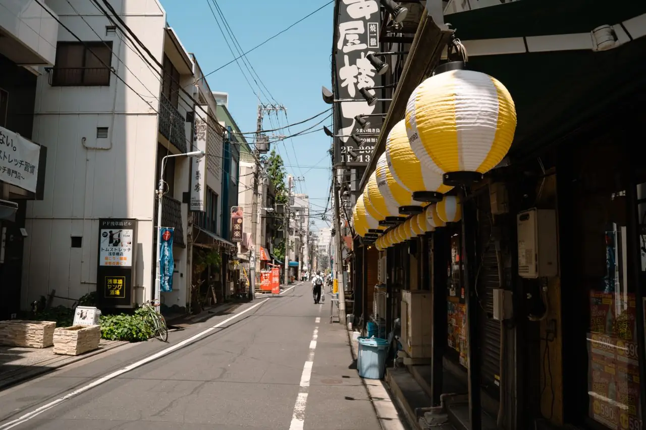 Quiet Tokyo side street lined with paper lanterns and small shops on a sunny day