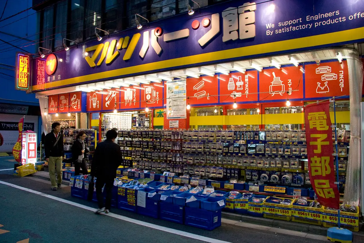Shoppers browsing an electronic parts store front lined with components in Akihabara at dusk