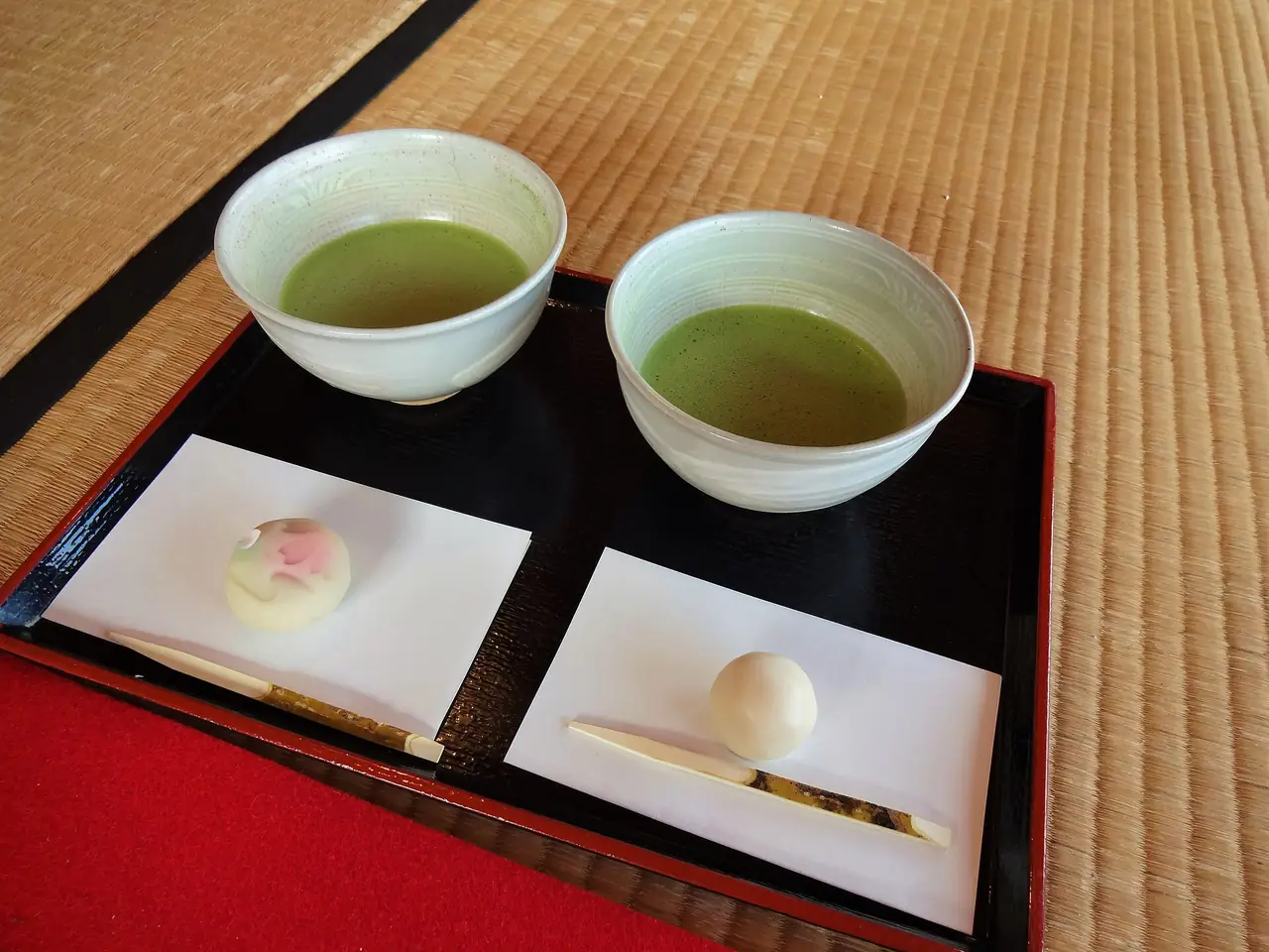 Two bowls of matcha with wagashi sweets on a lacquer tray on tatami