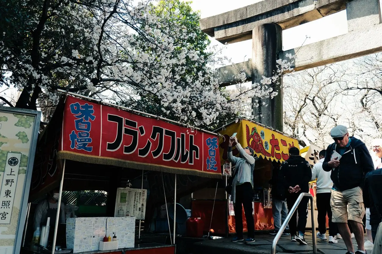 Festival food stalls under cherry blossoms beside the stone torii of Ueno Toshogu