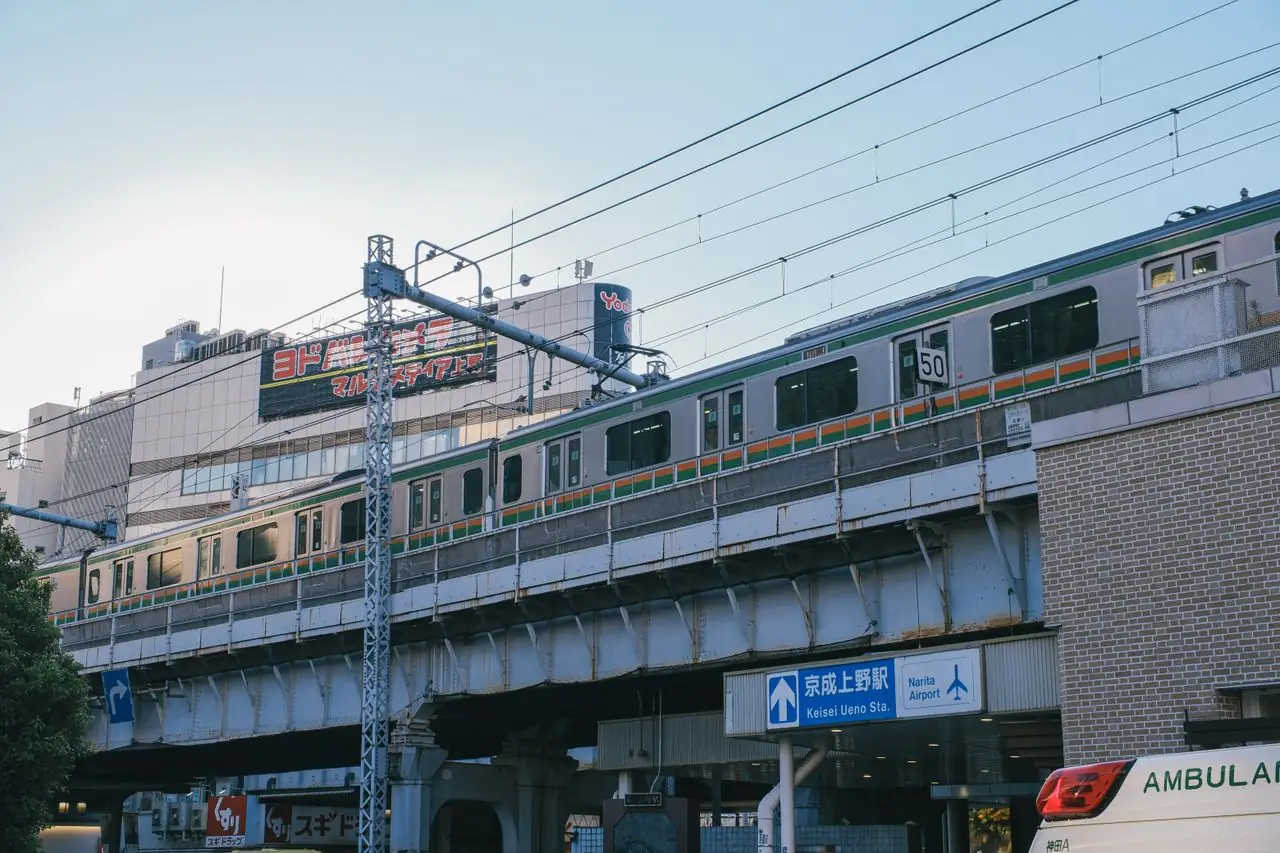 A JR train crosses the viaduct above the entrance sign for Keisei Ueno Station