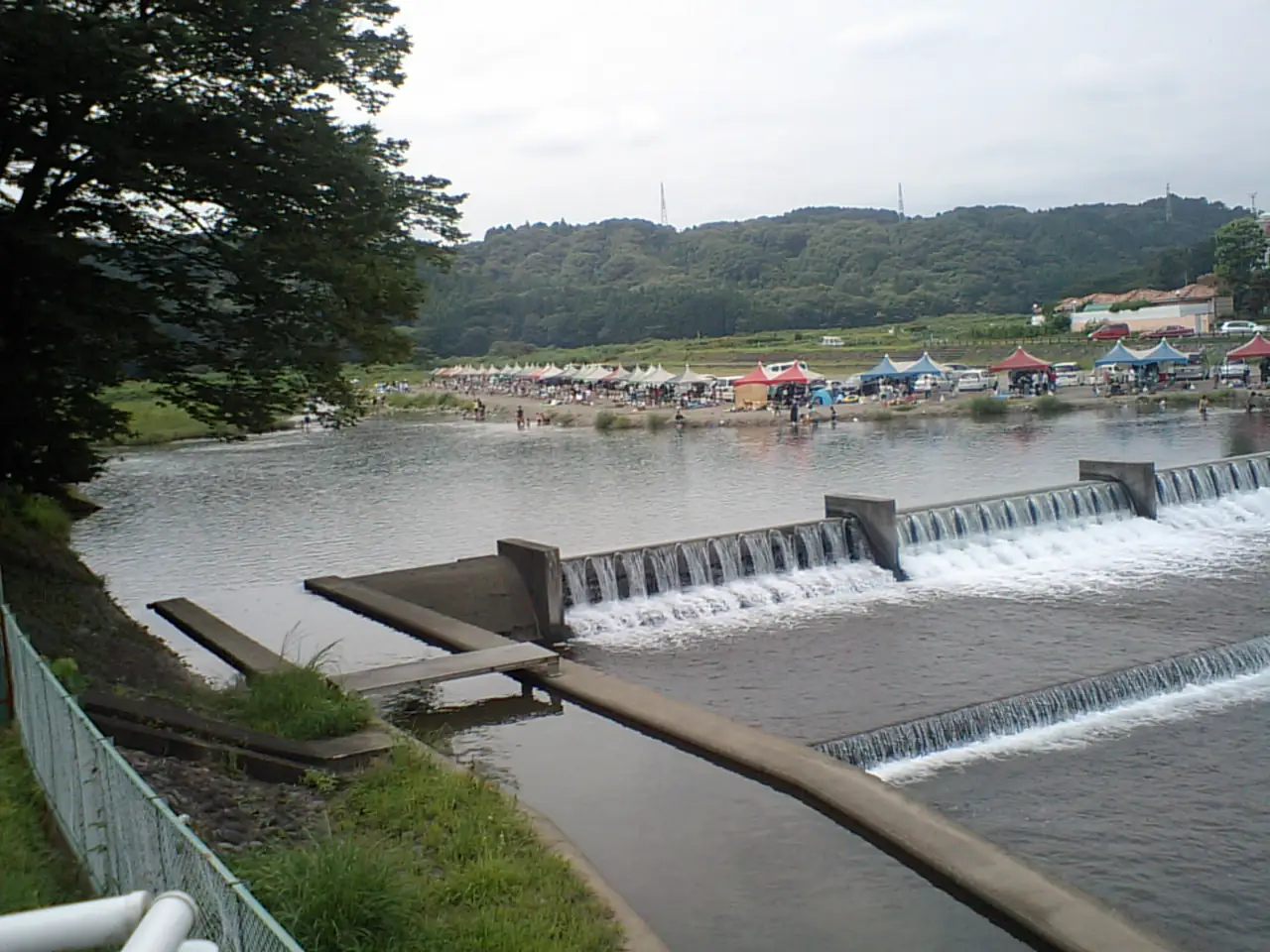 Canopies and tents along the Akigawa riverbank above a low weir in summer