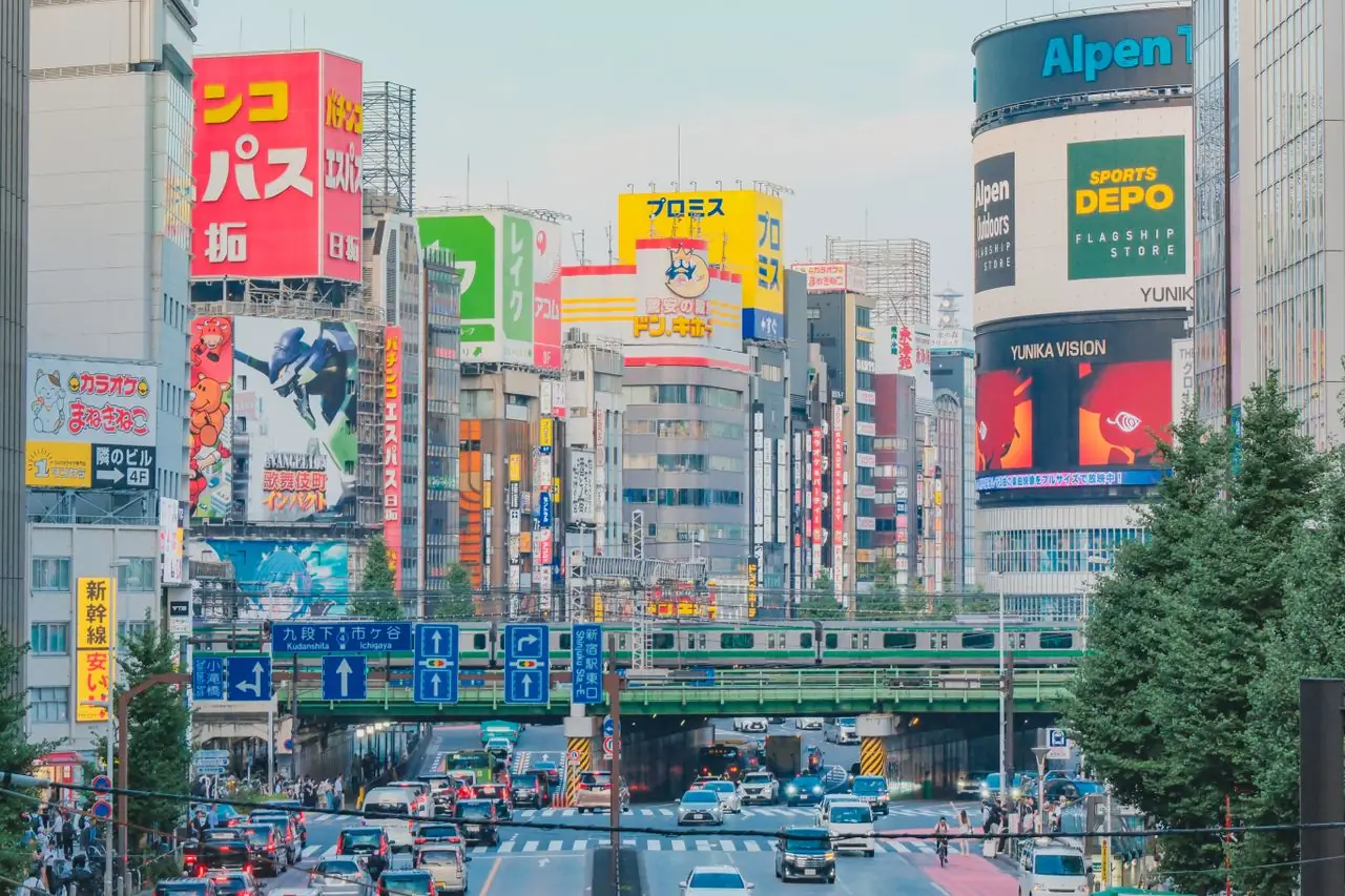 Billboards and traffic in Shinjuku beneath a JR railway bridge