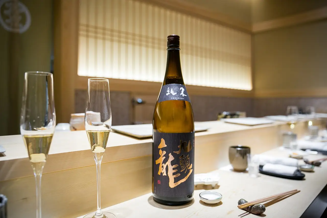 The pale wooden sushi counter at Sushi Saito in Tokyo, set with sake and glasses
