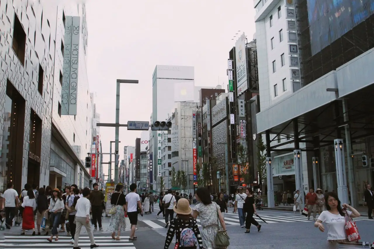 Shoppers crossing a wide avenue lined with department stores in Ginza, Tokyo