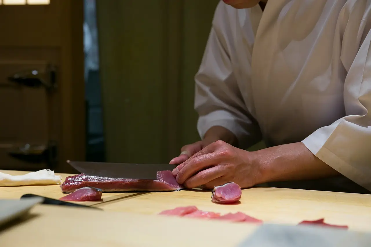 A chef at Sushi Saito slicing tuna on the wooden sushi counter