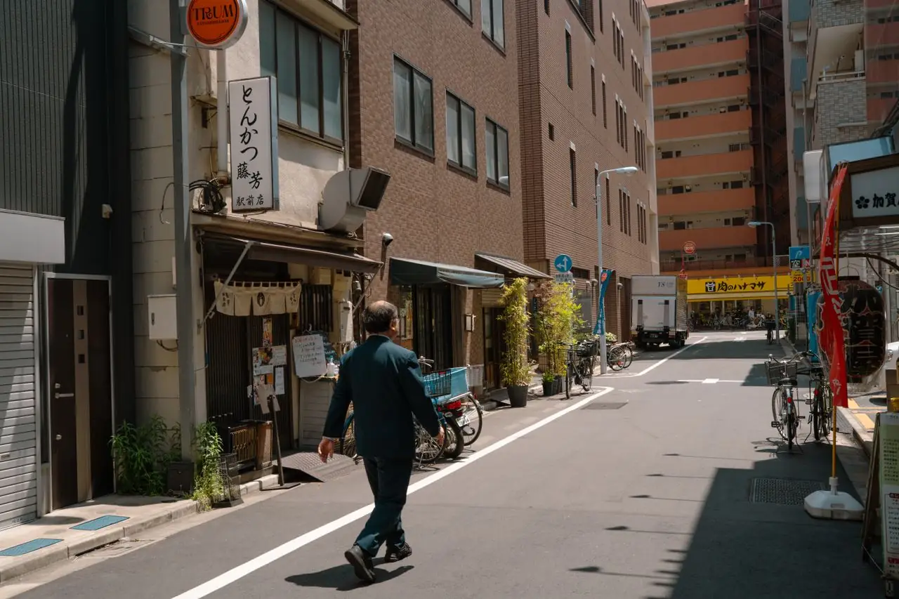 A lone pedestrian walking past small shops on a quiet Tokyo side street