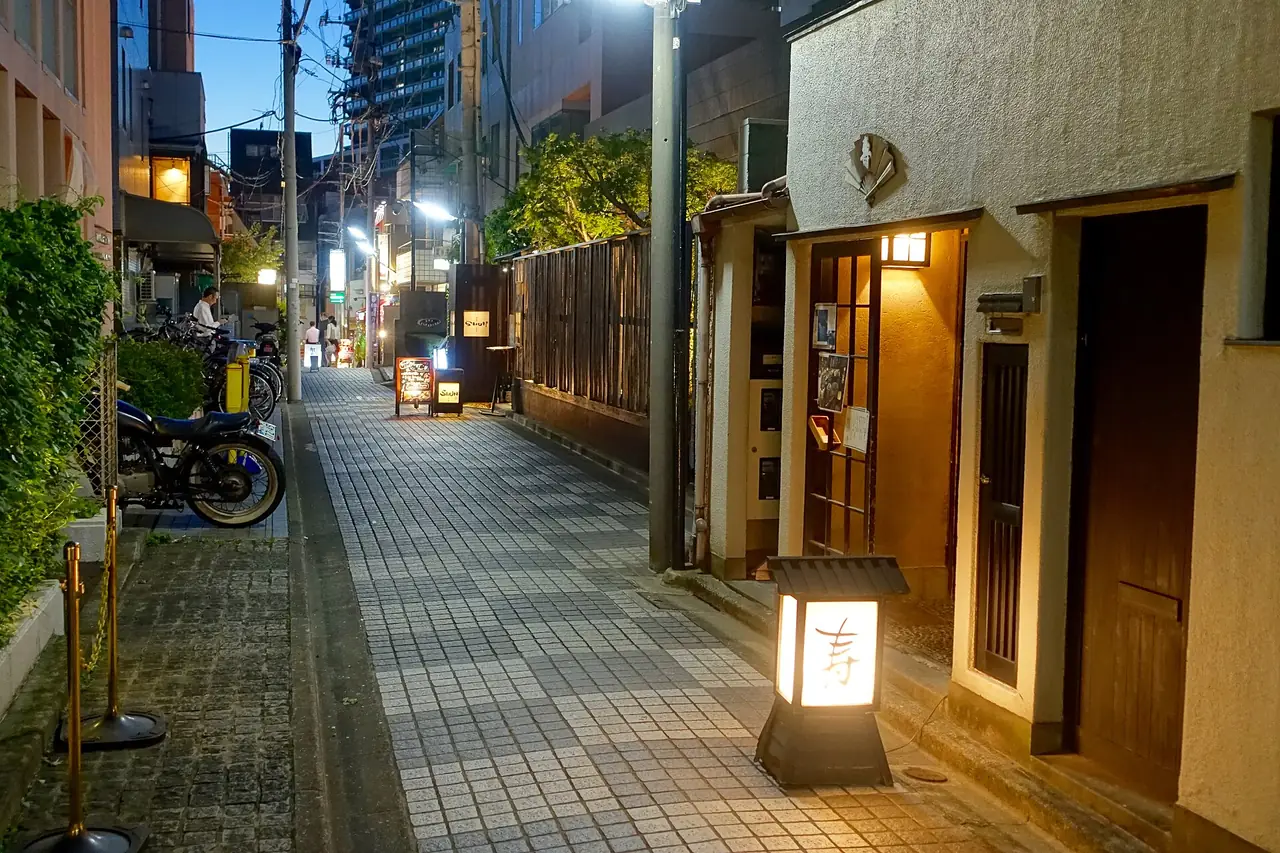 Quiet paved lane in Kagurazaka at dusk with a lit lantern by a restaurant door