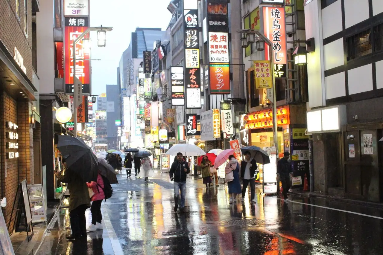 Pedestrians with umbrellas on a wet shopping street lined with Japanese signs on a rainy day