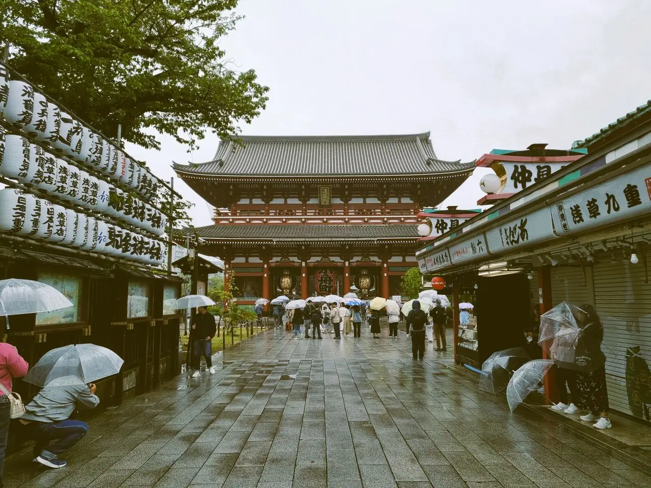 Visitors with umbrellas on a quiet, rain-soaked Nakamise-dori leading to Senso-ji