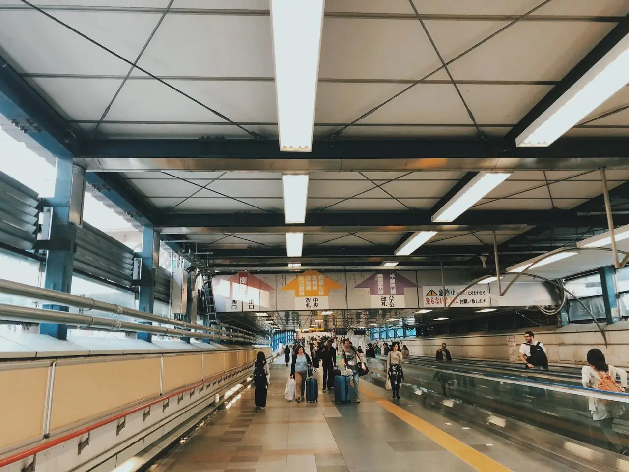 Travelers with luggage on a long connecting walkway inside Shibuya Station