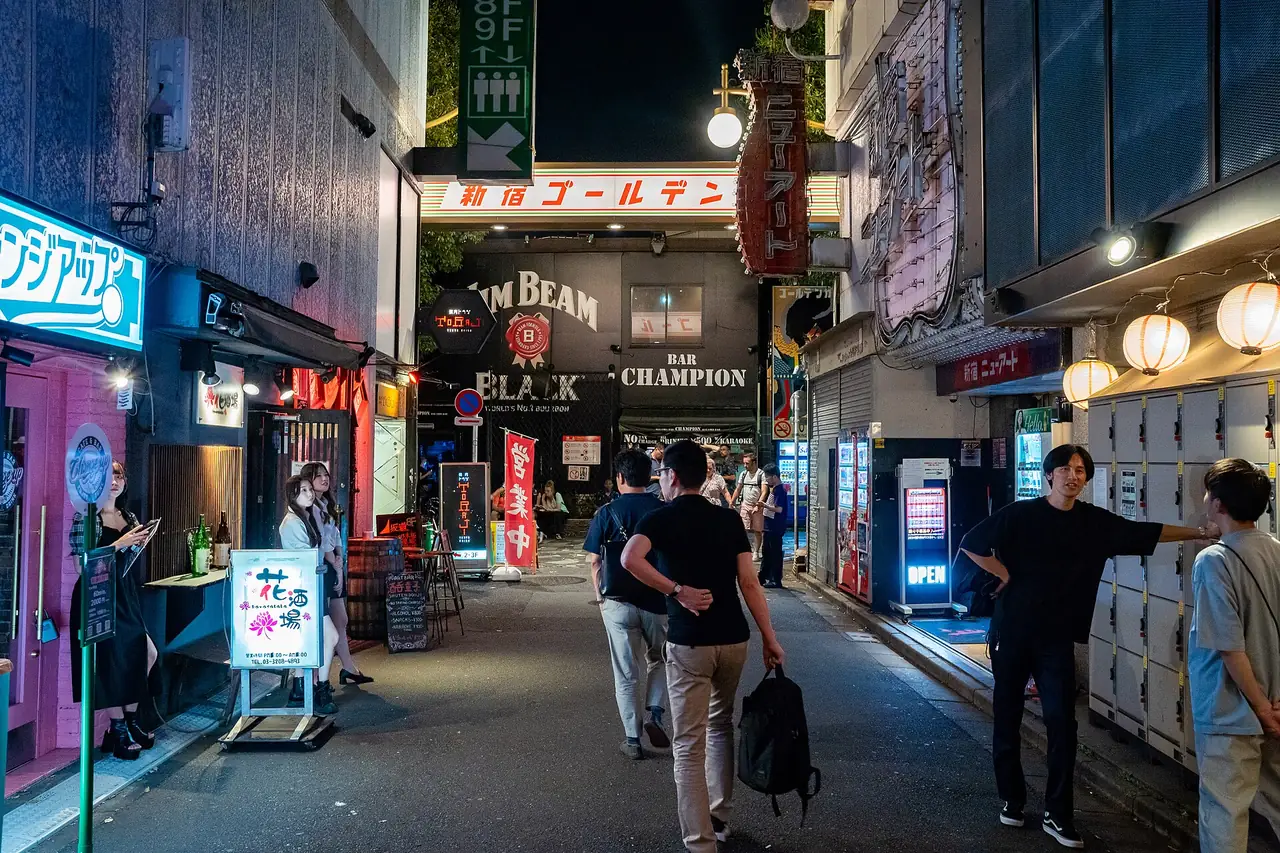Visitors walking under the Shinjuku Golden Gai entrance sign at night