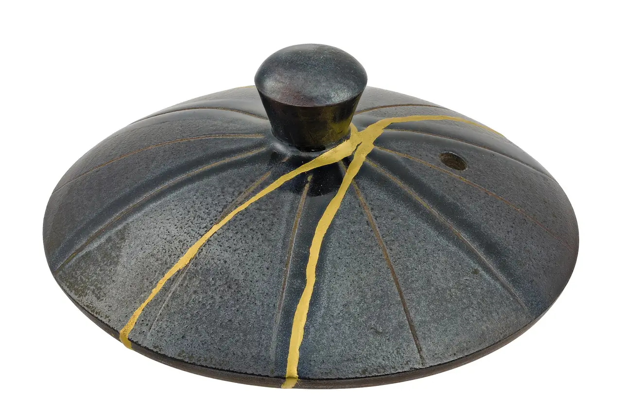 A Japanese teapot lid repaired with gold kintsugi seams along its cracks
