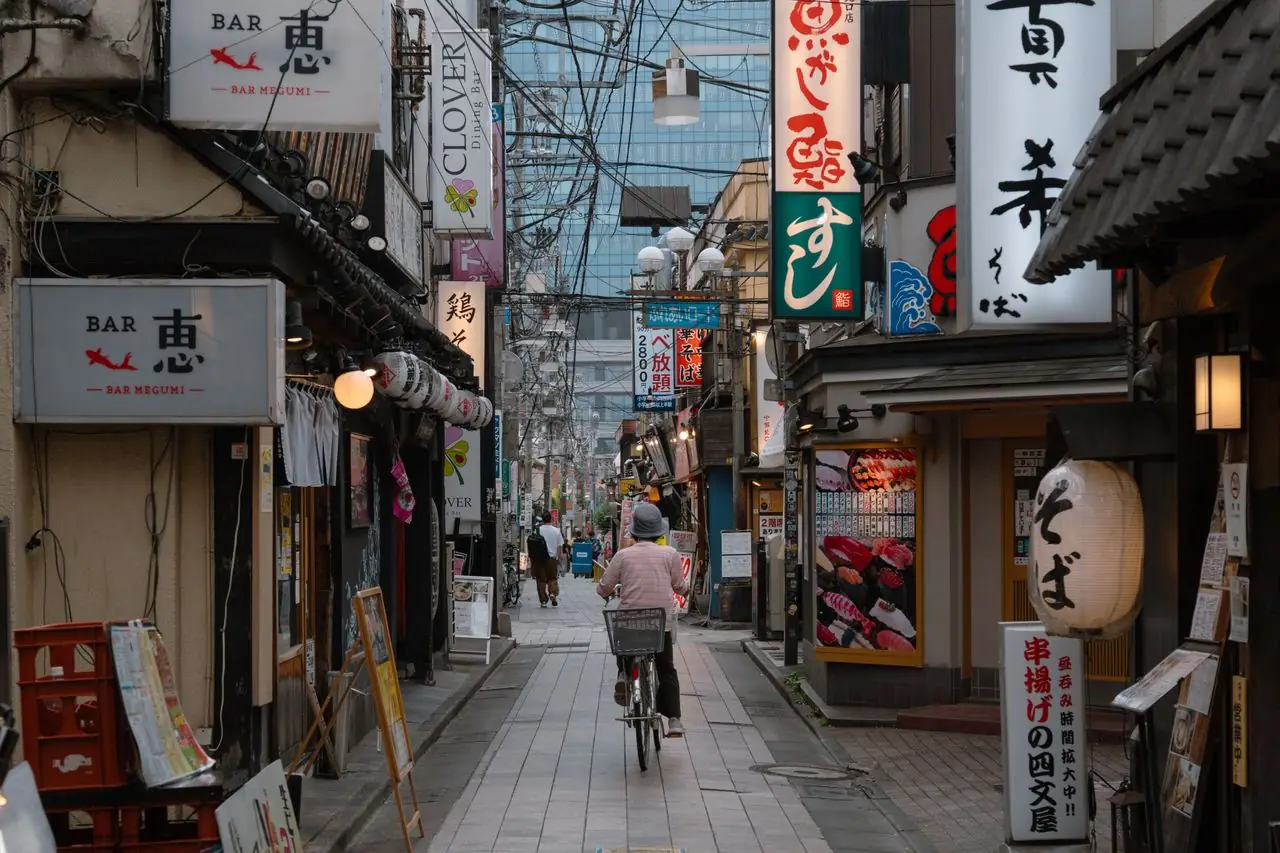A cyclist riding down a Tokyo backstreet lined with small restaurants and bars