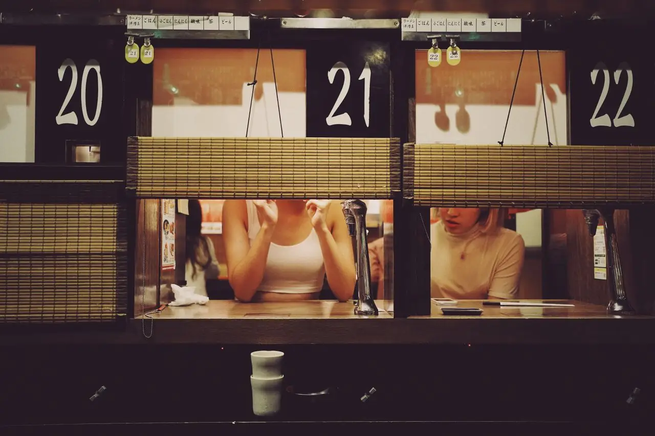 Diners in numbered solo booths with bamboo blinds at an Ichiran ramen counter