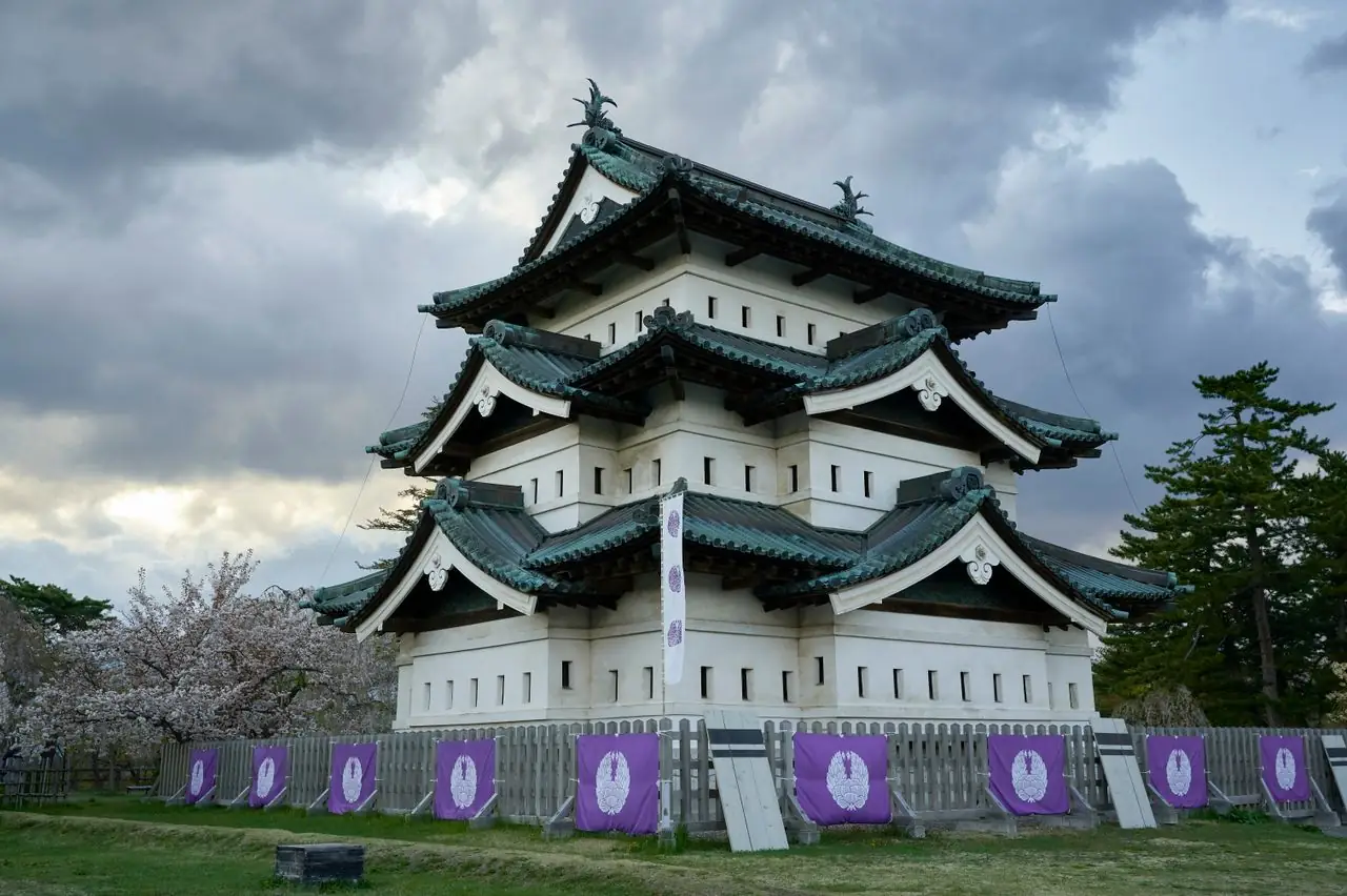 Hirosaki Castle keep with cherry trees in bloom under a cloudy spring sky
