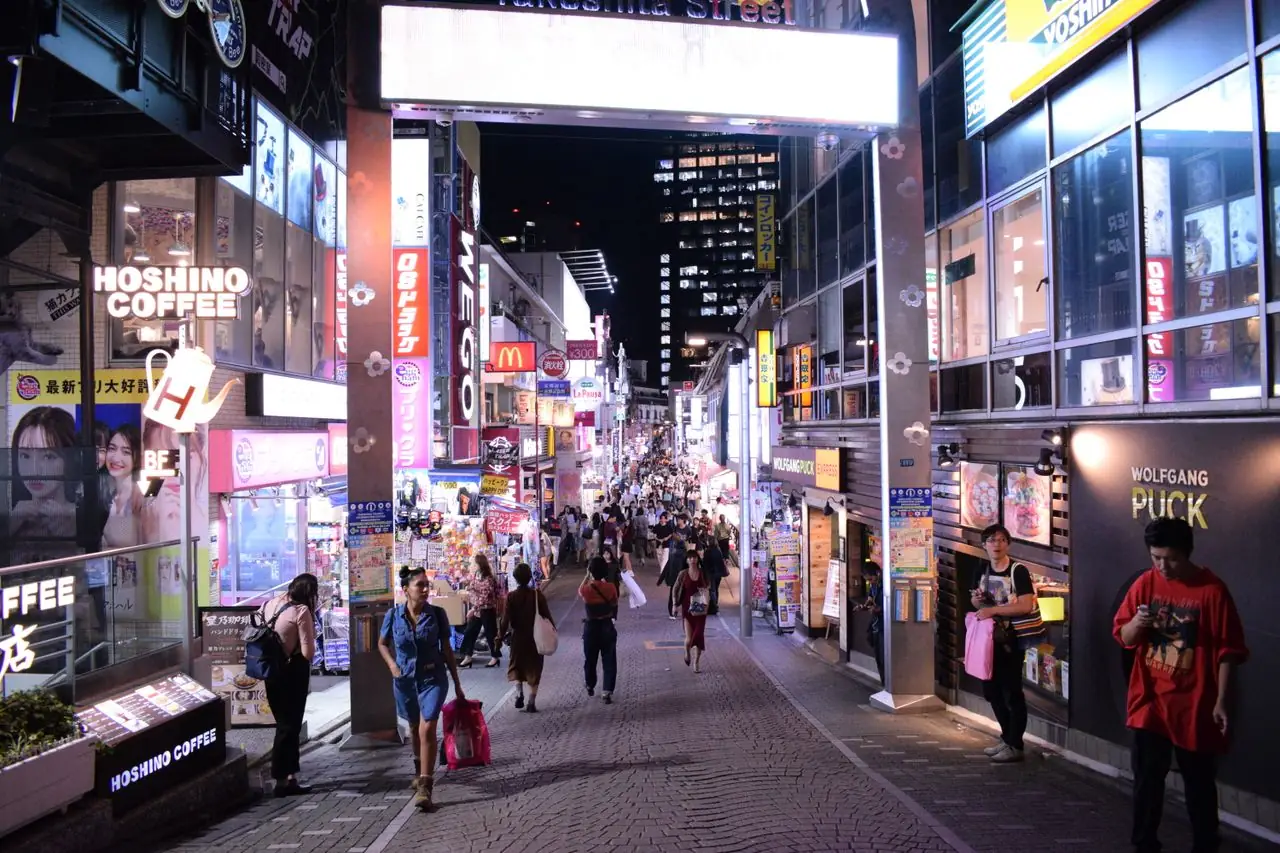 Shoppers walking down Takeshita Street in Harajuku at night under lit shop signs