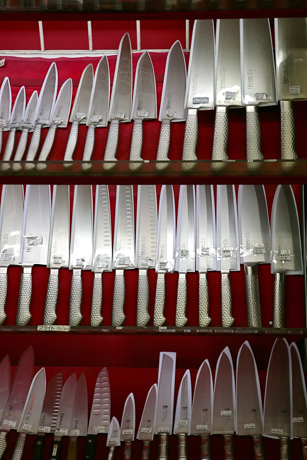 Rows of Japanese kitchen knives on red display boards in a Tokyo knife shop