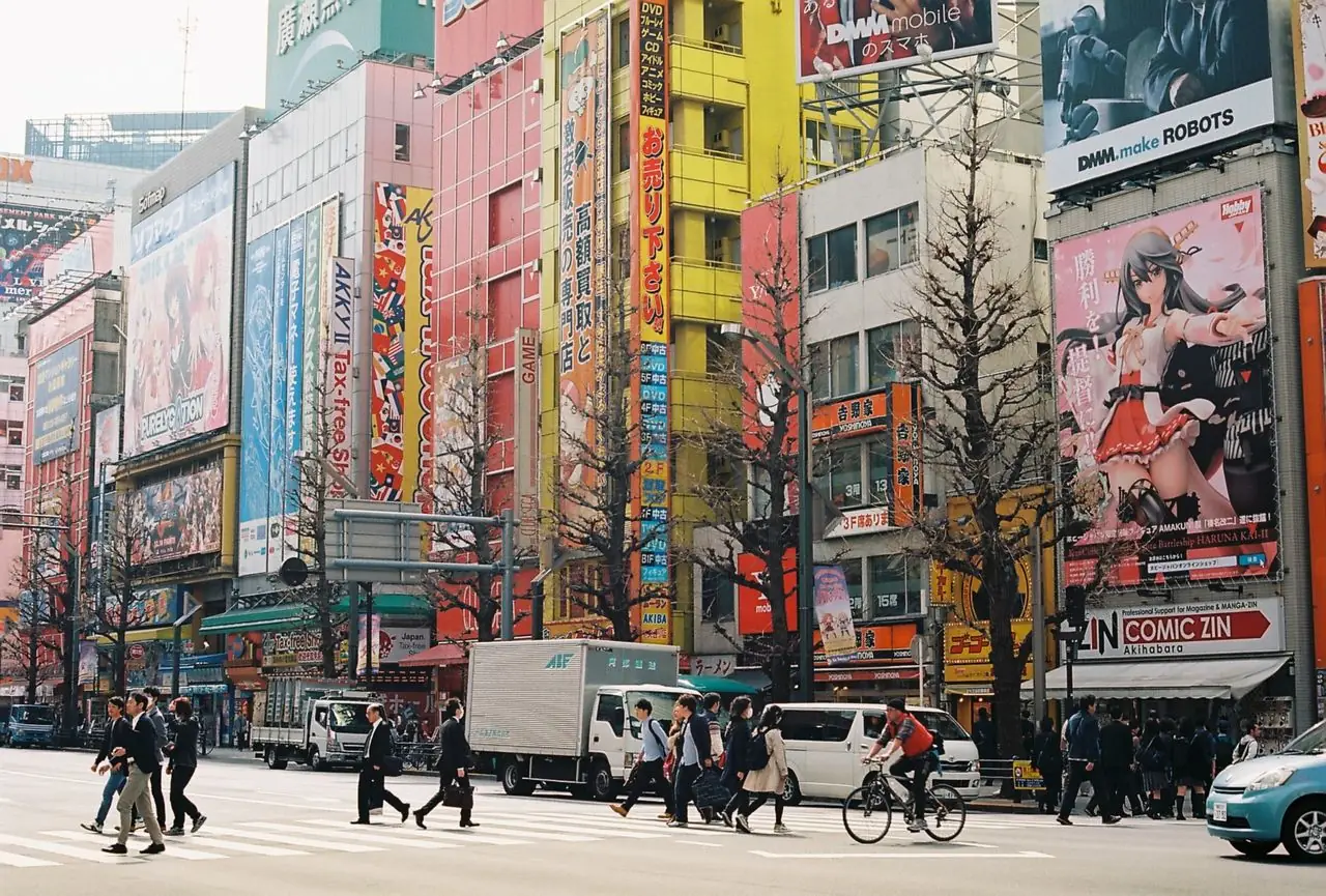 Pedestrians on a busy Akihabara street lined with anime and electronics billboards