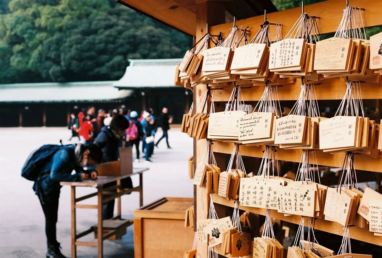 Visitors writing wooden ema prayer plaques beside the main courtyard at Meiji Shrine
